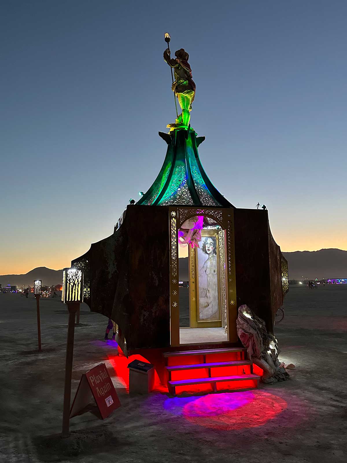 Ornate illuminated shrine with figure holding torch at dusk
