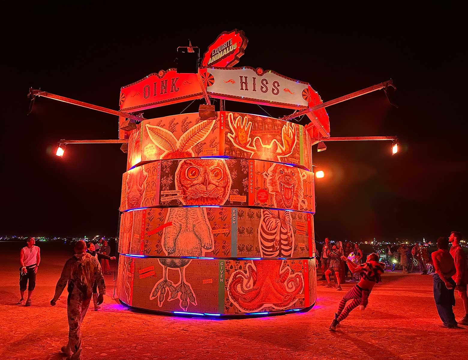 Illuminated cylindrical carnival art piece with animal illustrations at night