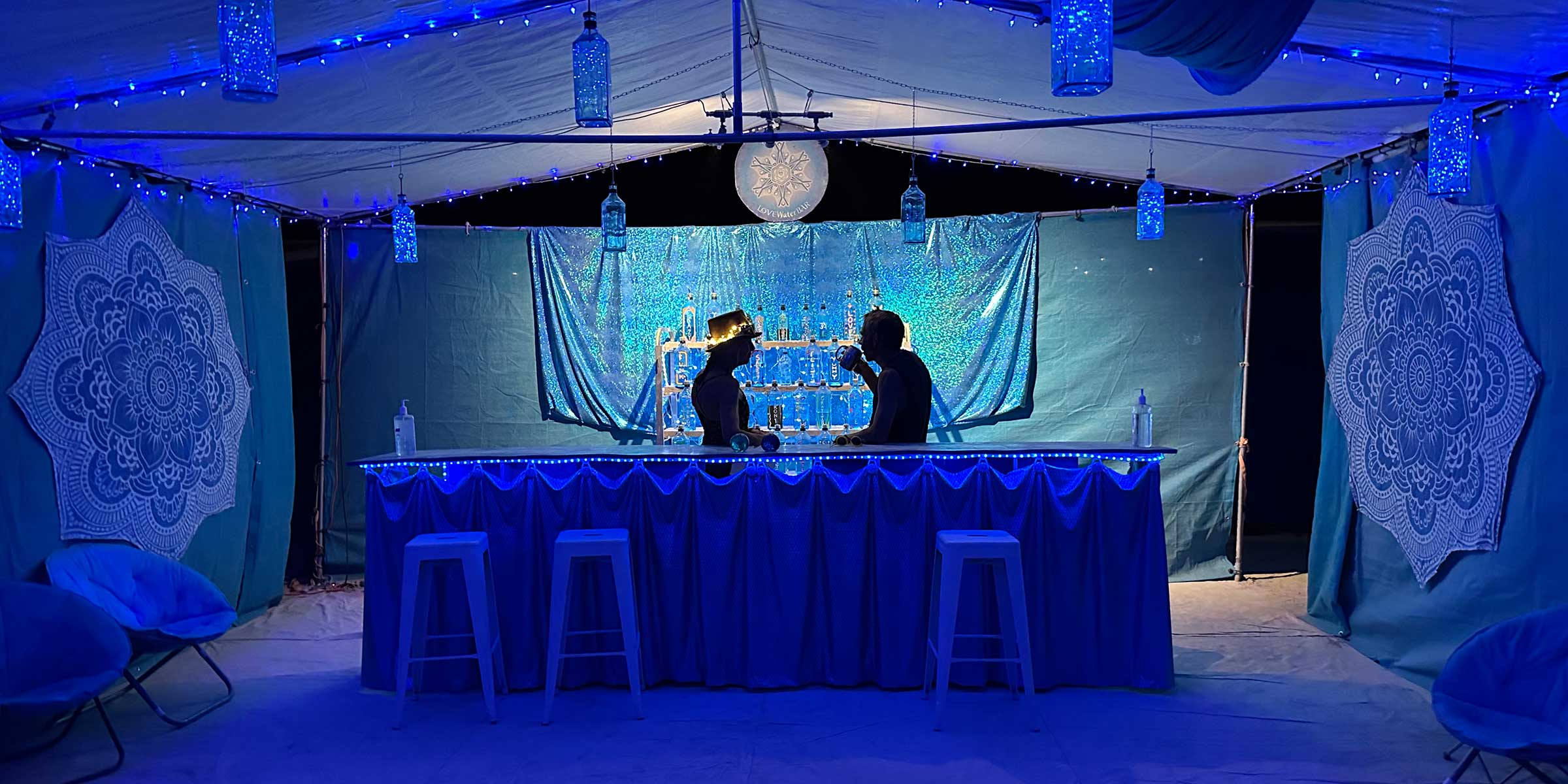 Two silhouettes at a blue LED-lit camp bar