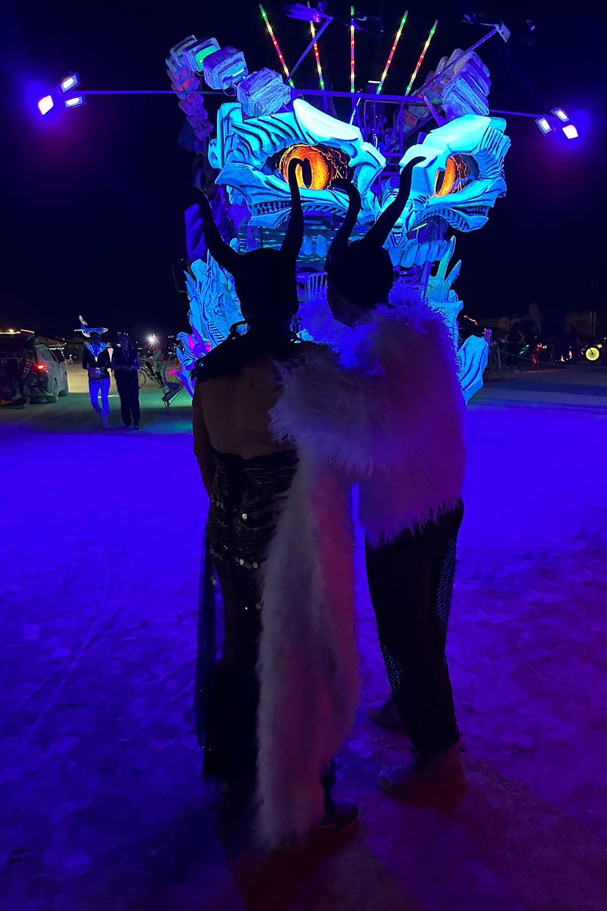 Two horned costumed figures before glowing blue dragon art car