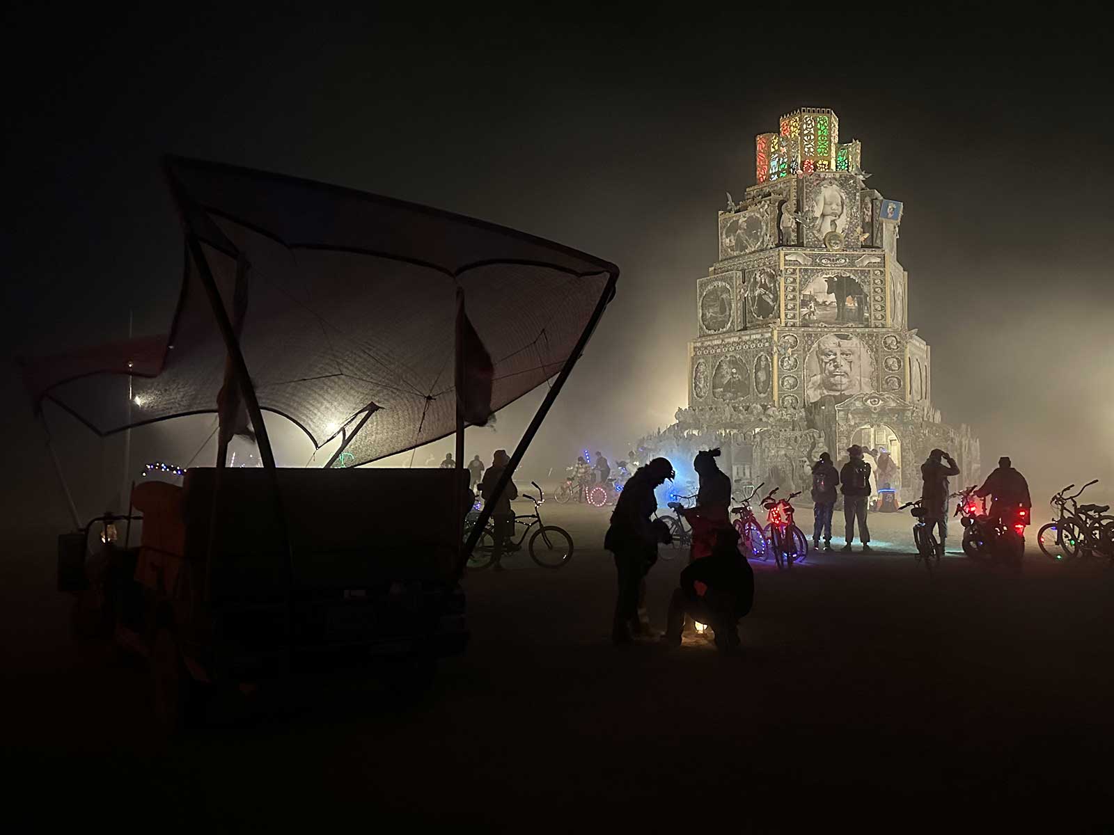 Massive ornate tiered tower glowing through dusty night playa