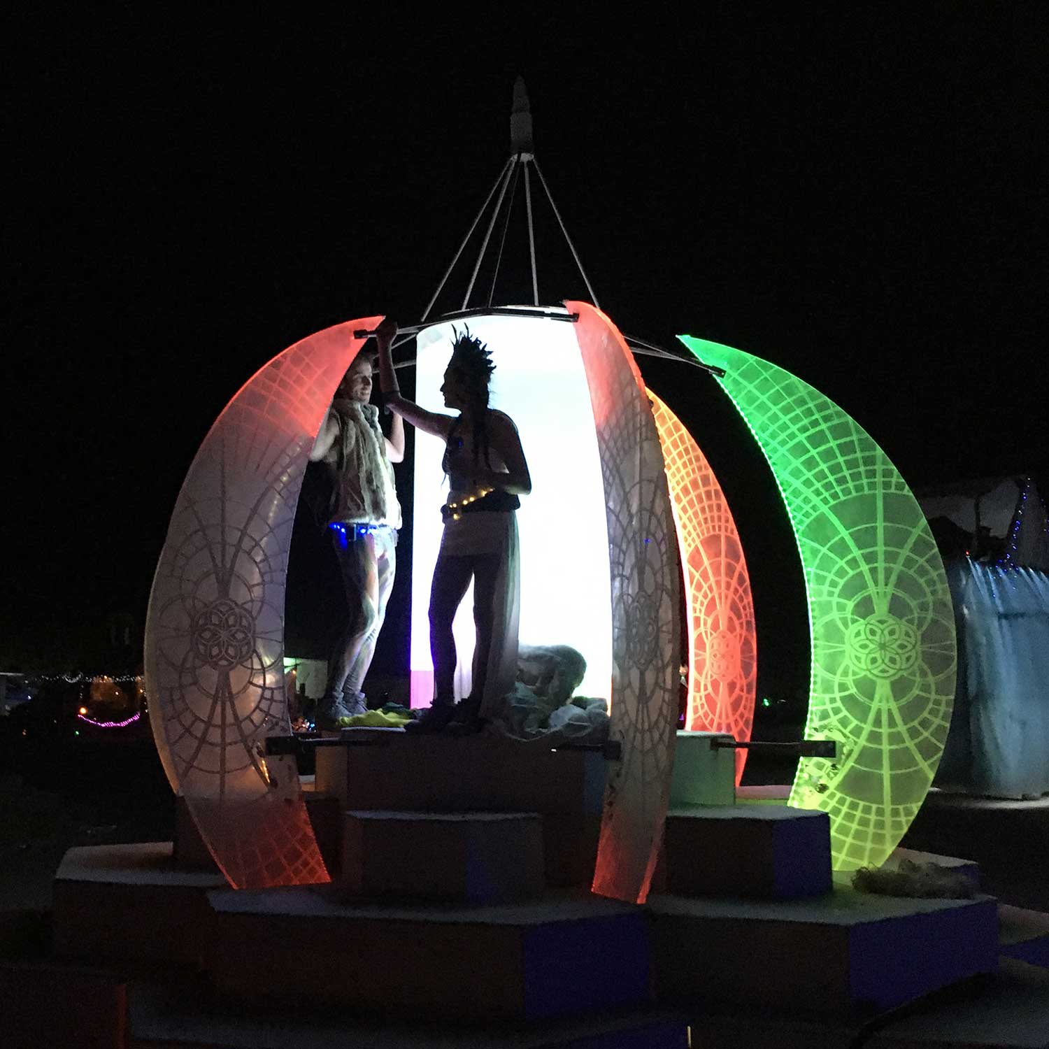 Two people silhouetted inside glowing colorful orb sculpture at night
