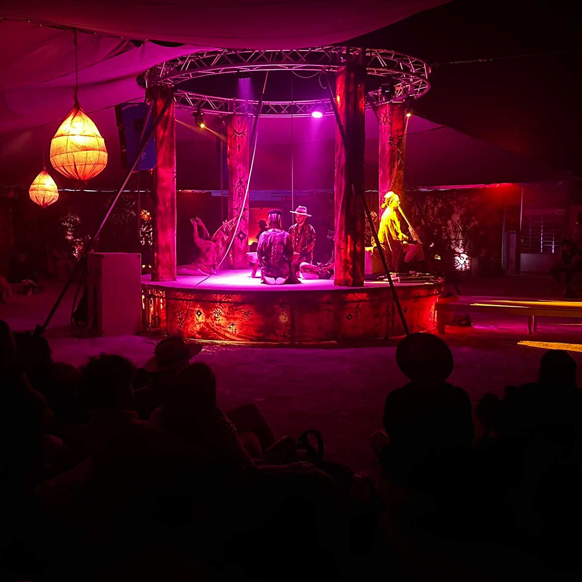 Performers on illuminated circular stage under pink tent lighting