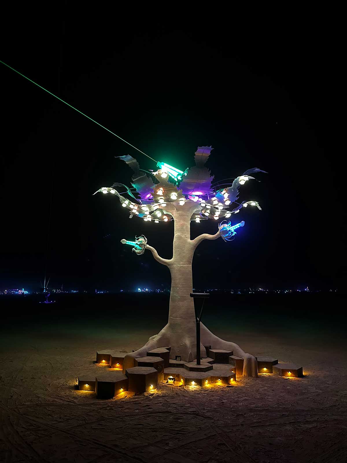 White tree sculpture with glowing bulbs and green laser beam