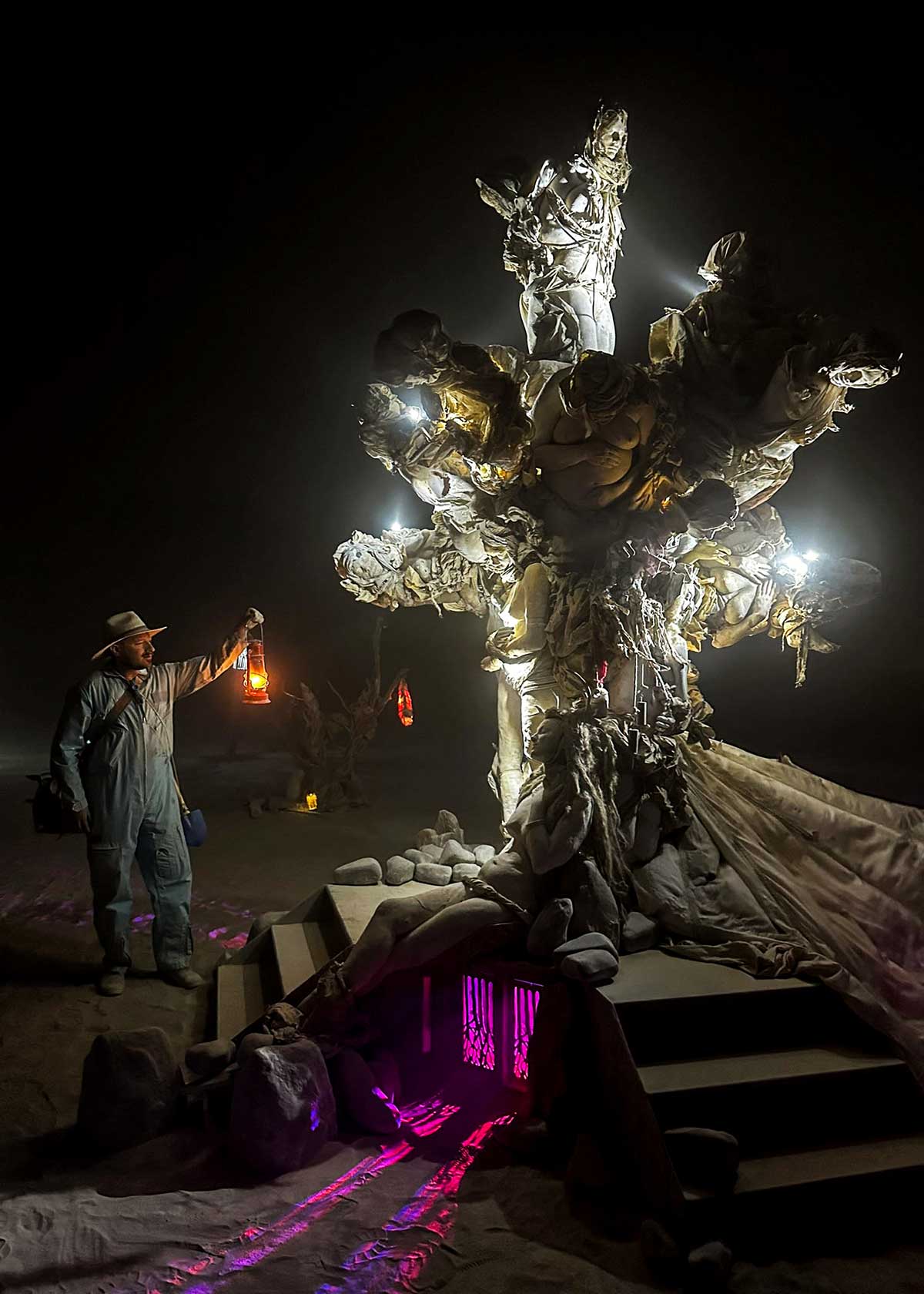 Man with lantern beside illuminated white tree sculpture at night