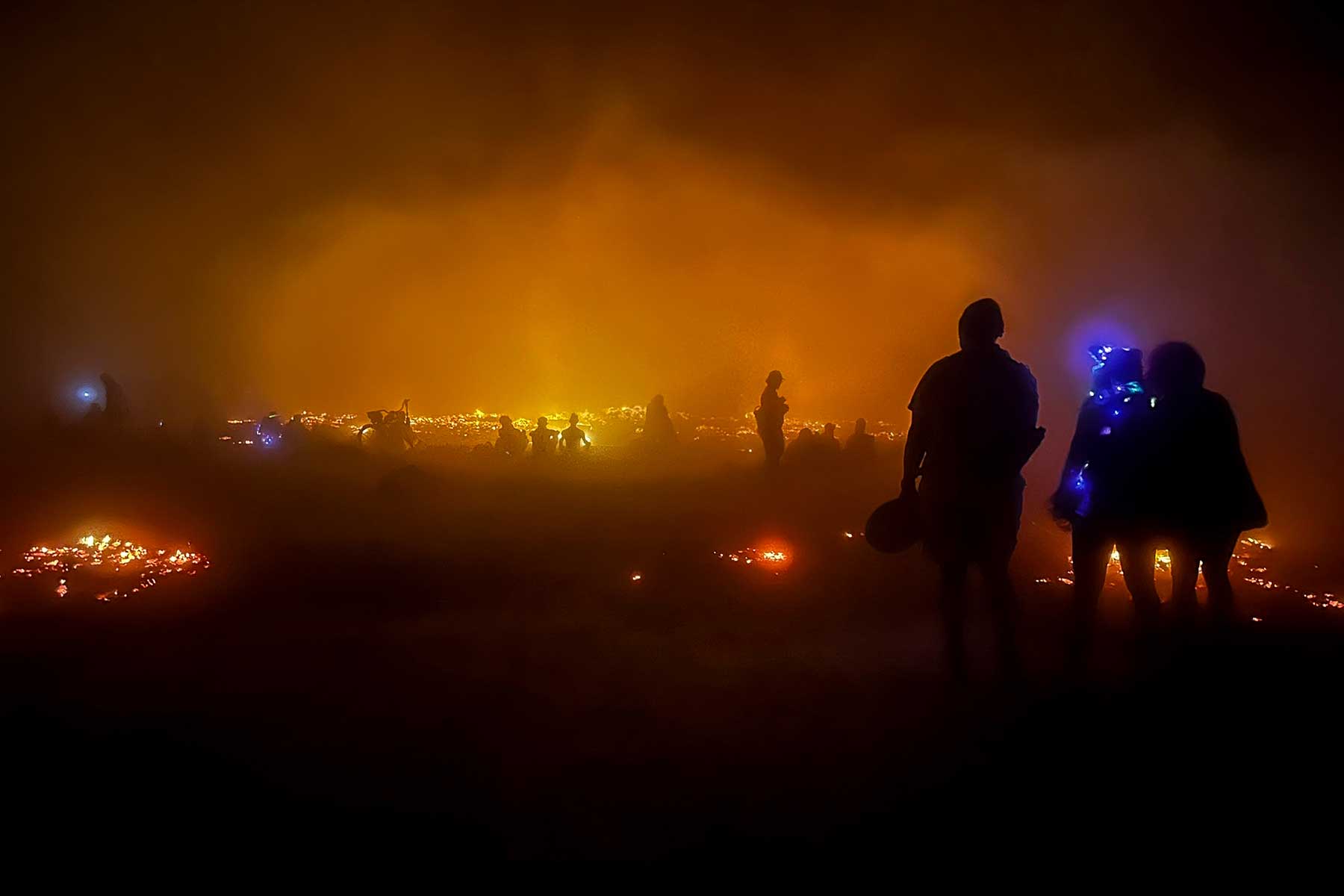 Silhouetted crowd walking through fire smoke and orange glow