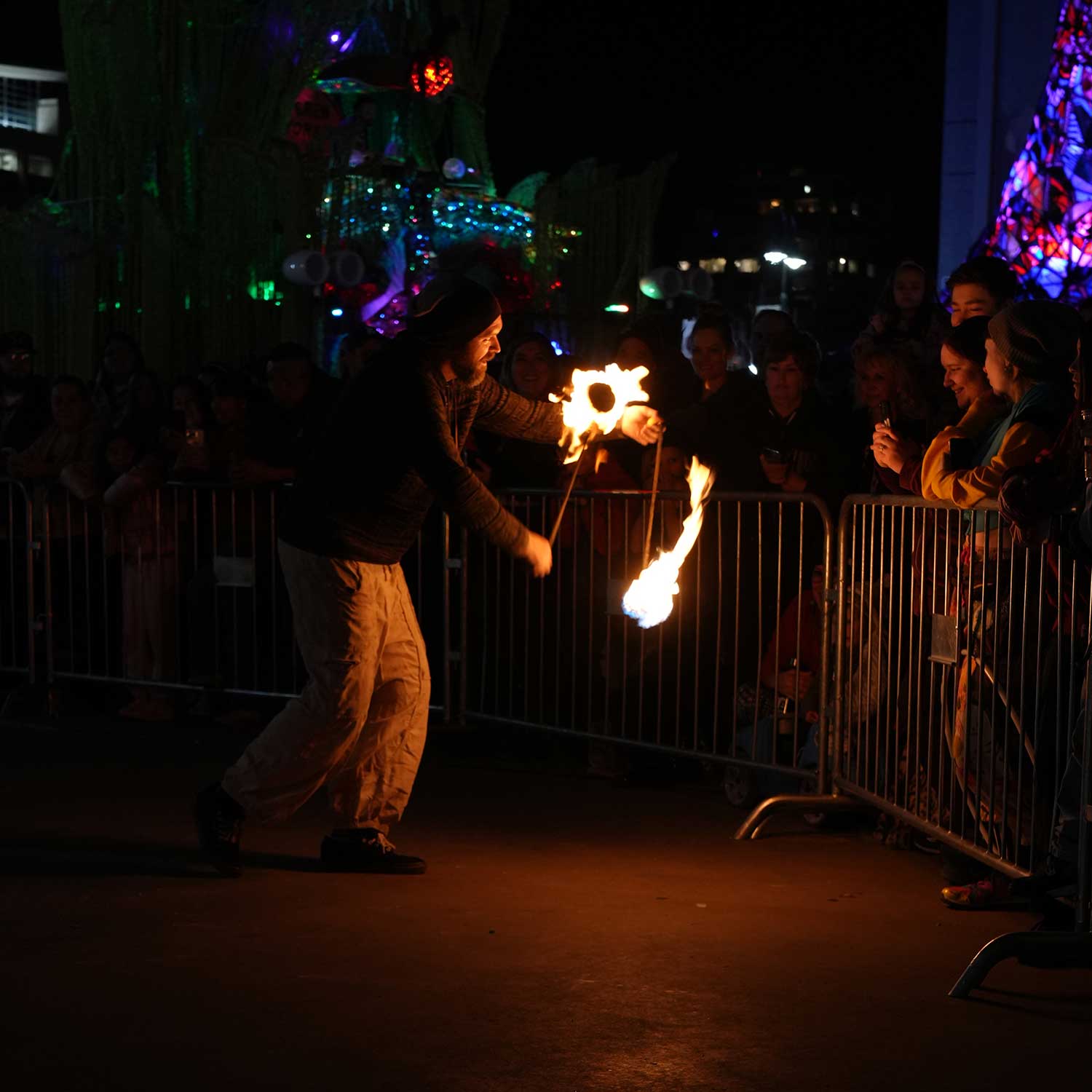 Fire performer with flaming props near crowd at night festival