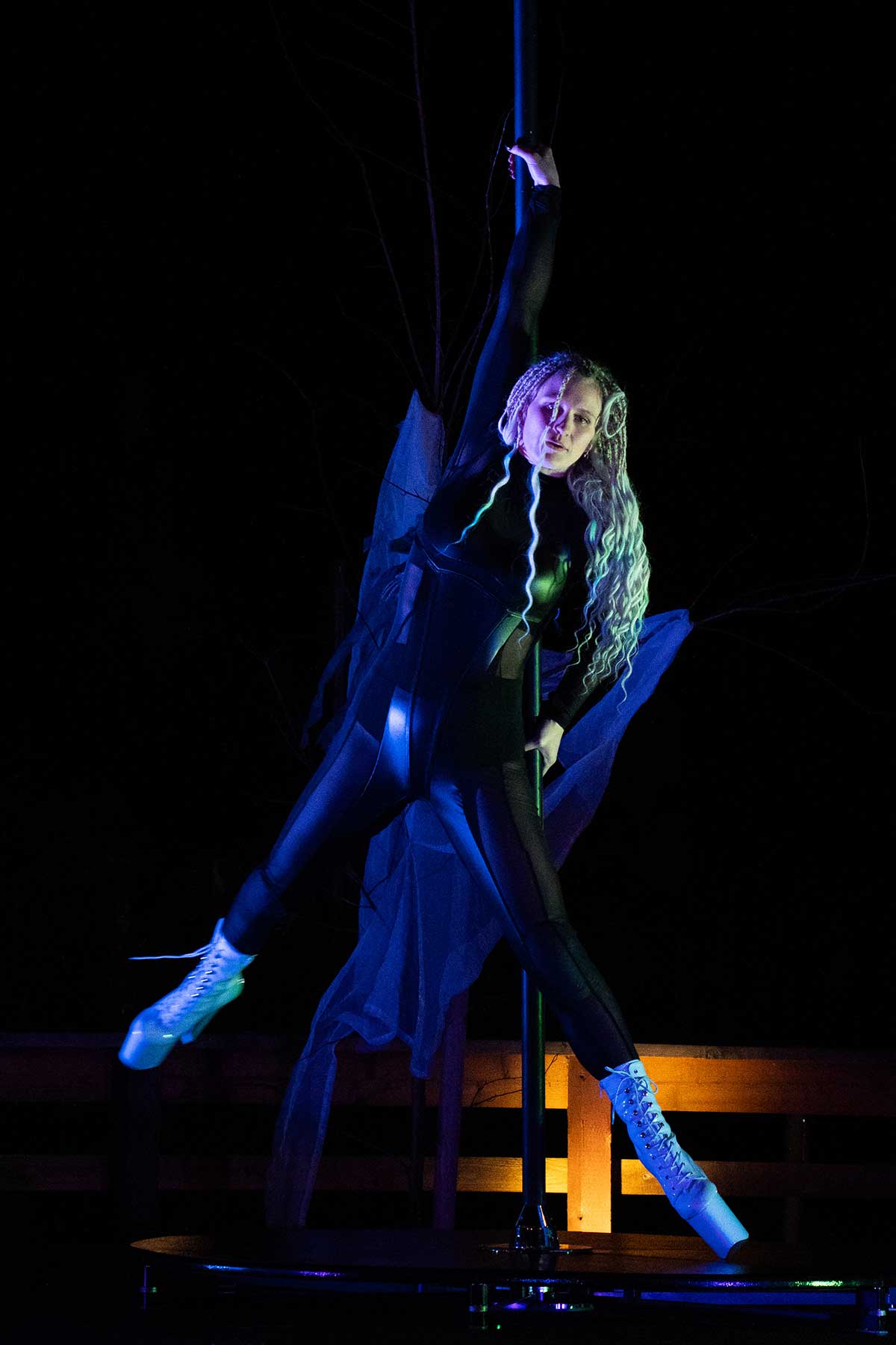 Curly-haired pole dancer in black outfit under blue stage light