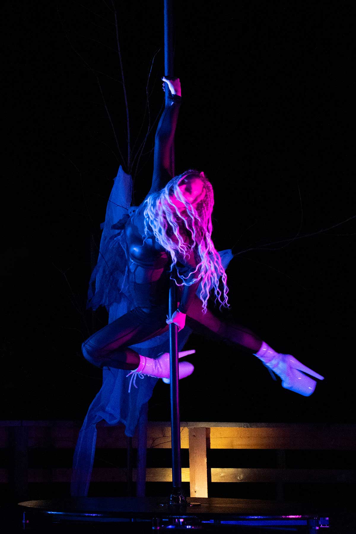 Pole dancer in dark wings costume under pink stage light