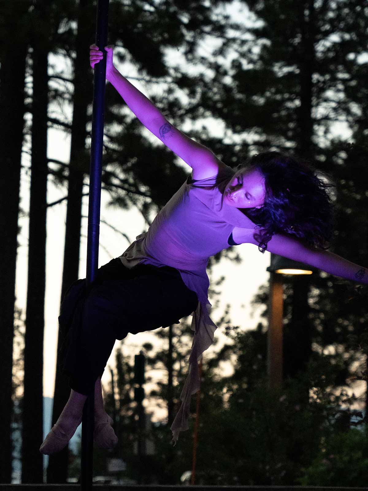 Pole dancer leaning back from outdoor pole at dusk