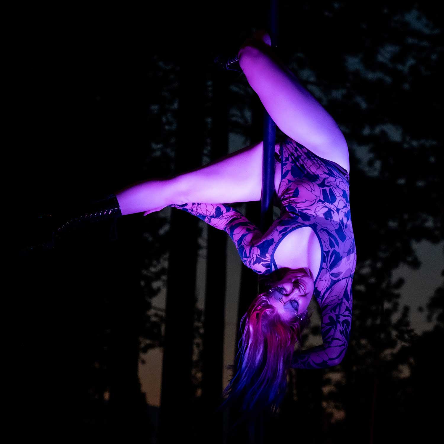 Floral-suited pole dancer inverted on outdoor pole at dusk