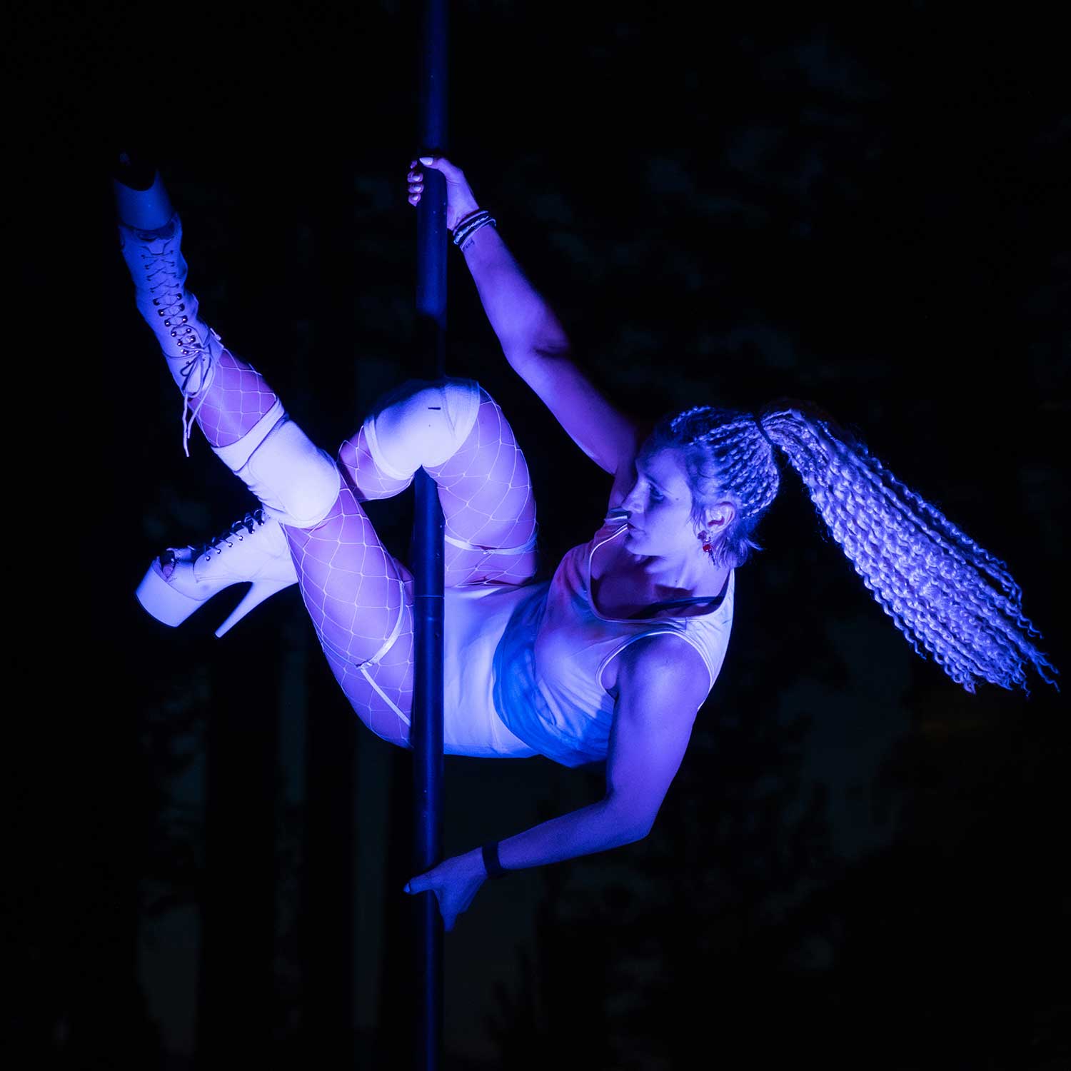 Pole dancer in white suspended horizontally on pole in darkness