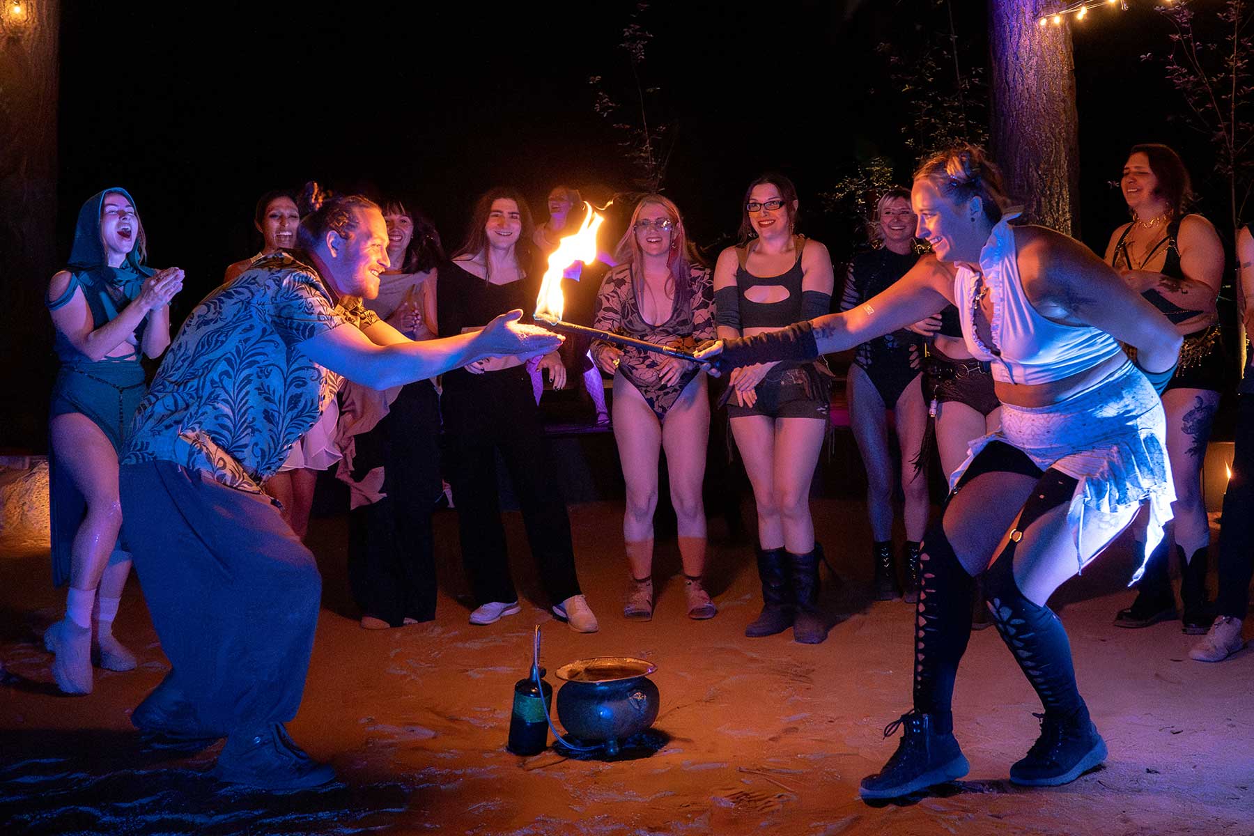 Two performers passing a flaming sword before cheering crowd outdoors