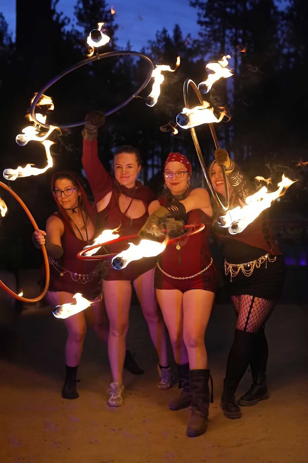 Four fire performers posing together with flaming hoops at dusk
