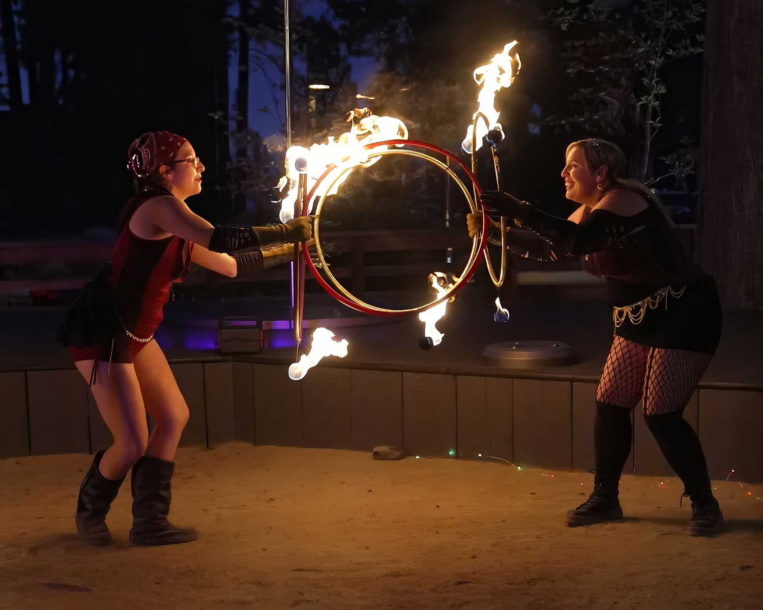 Two performers together spinning a shared flaming hoop at night