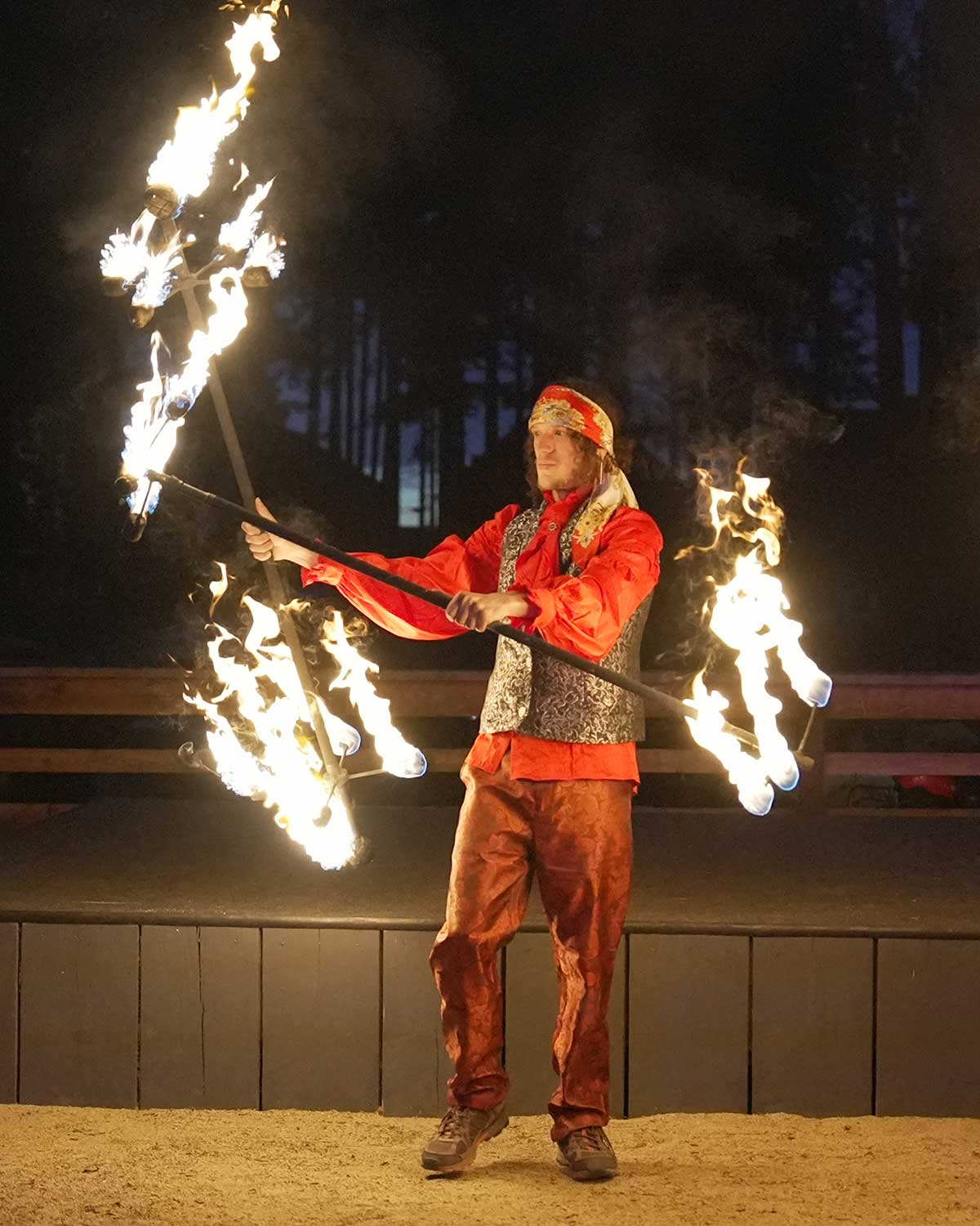 Costumed performer spinning fire staff in red regalia at night