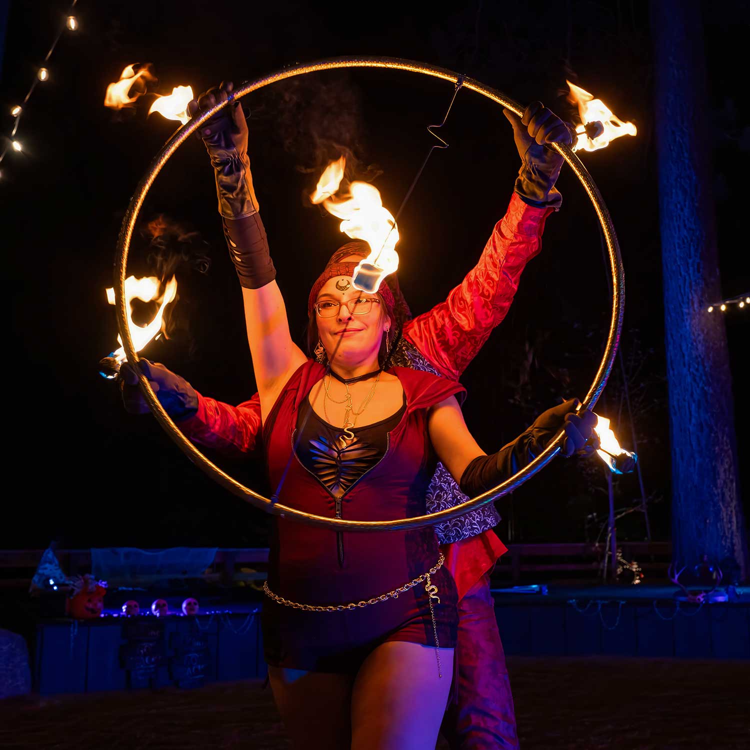 Fire hoop performer raising large flaming hoop overhead at night