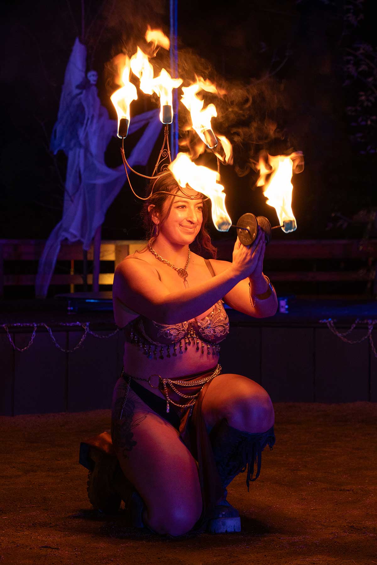 Kneeling fire performer with flaming headdress and fans at night