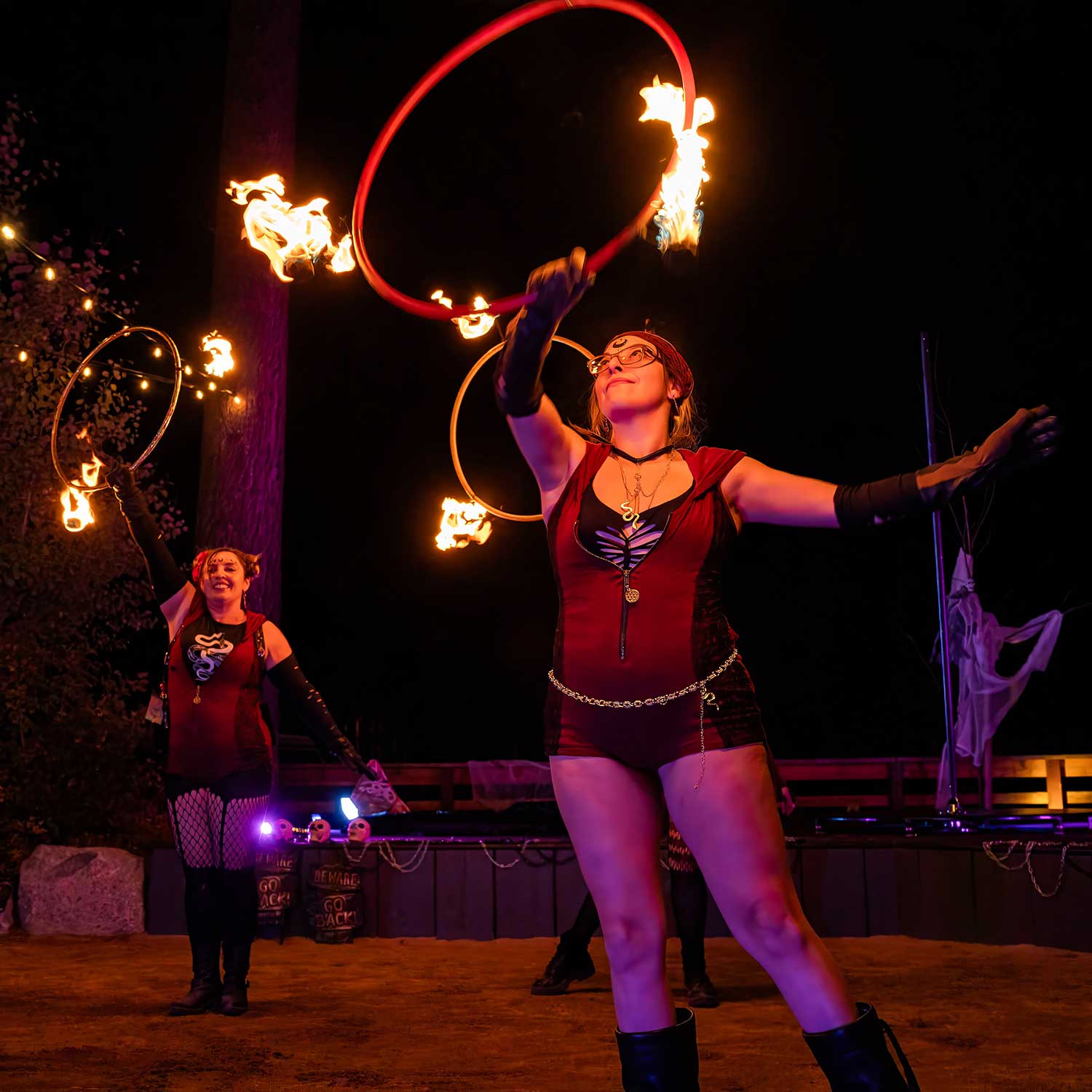 Two fire hoop dancers spinning flaming rings at outdoor night event
