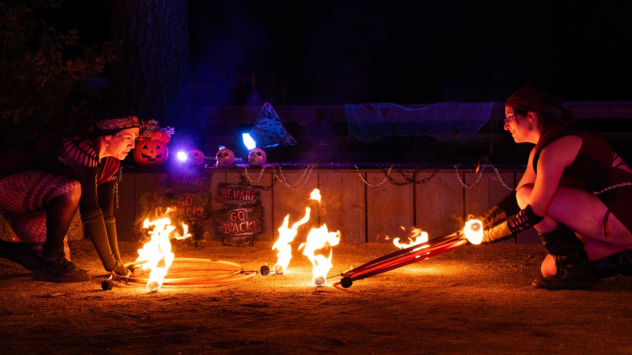 Two fire performers crouching with flaming props at Halloween event