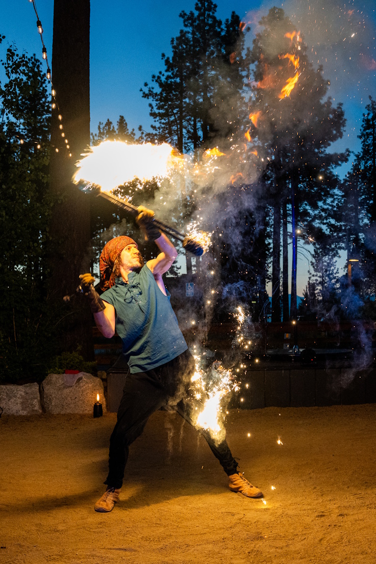 Male performer blowing fire with sparks cascading at outdoor dusk event