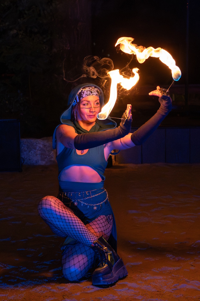 Kneeling fire poi performer in blue light at outdoor night event