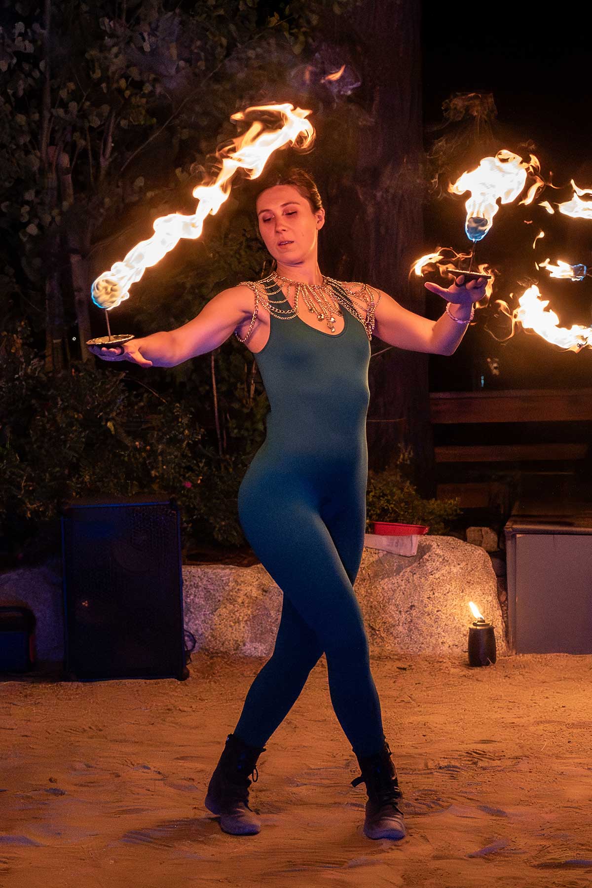 Fire performer in teal bodysuit spinning fans with arms outstretched