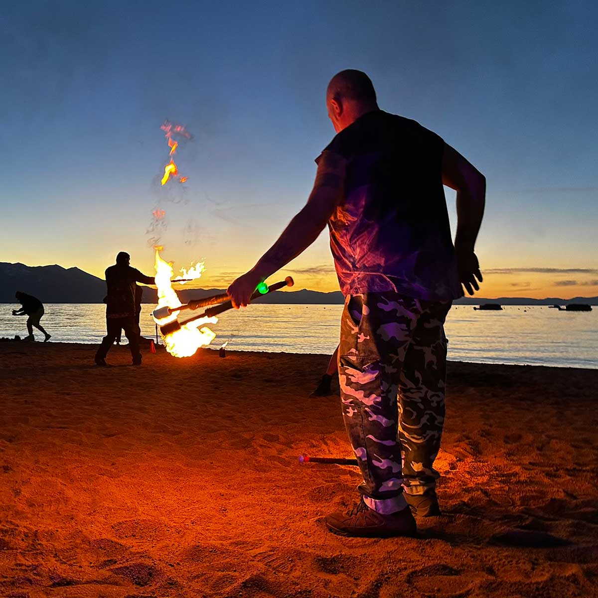 Fire performer spinning baton on beach at sunset with lake view