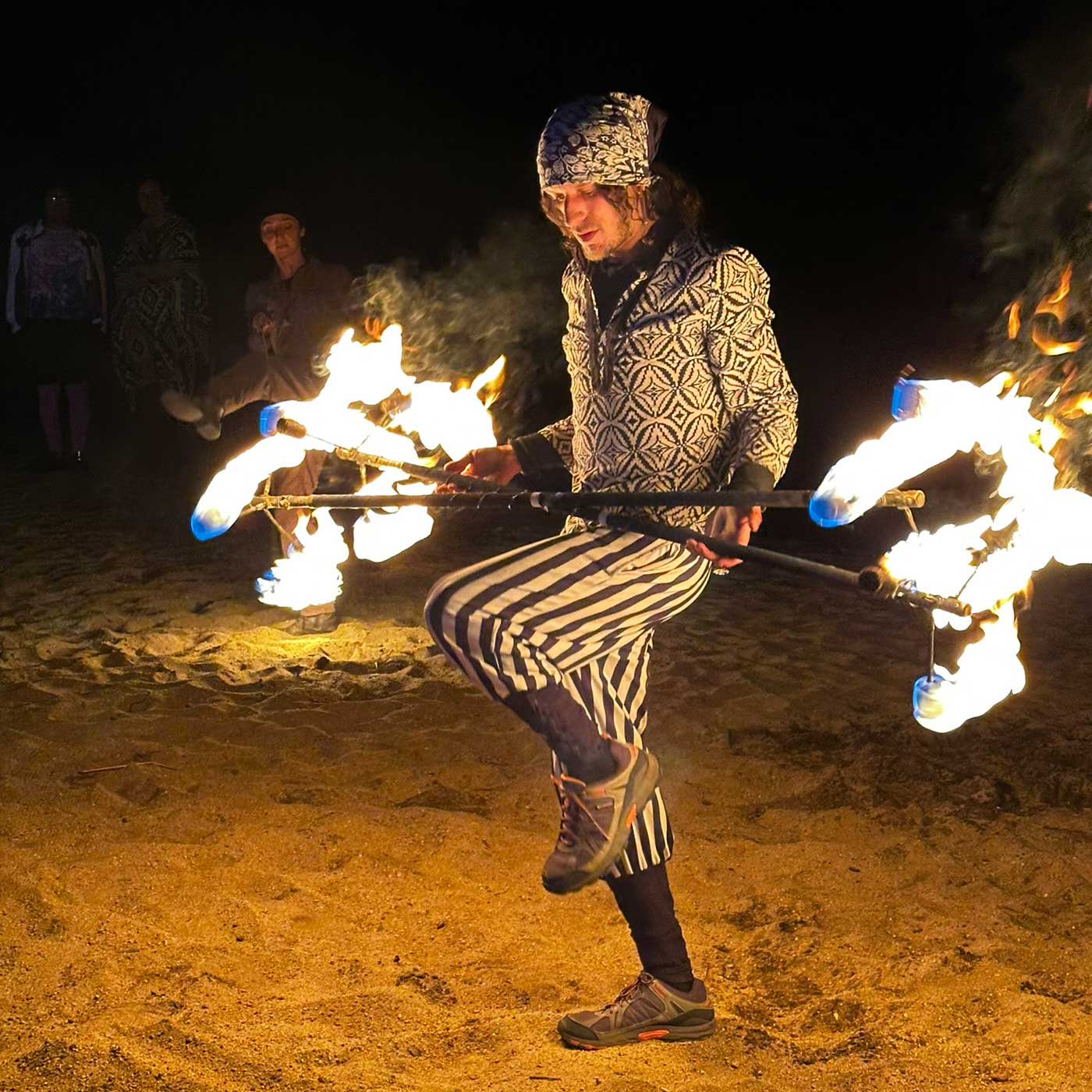 Fire staff performer on one leg spinning at sandy outdoor event