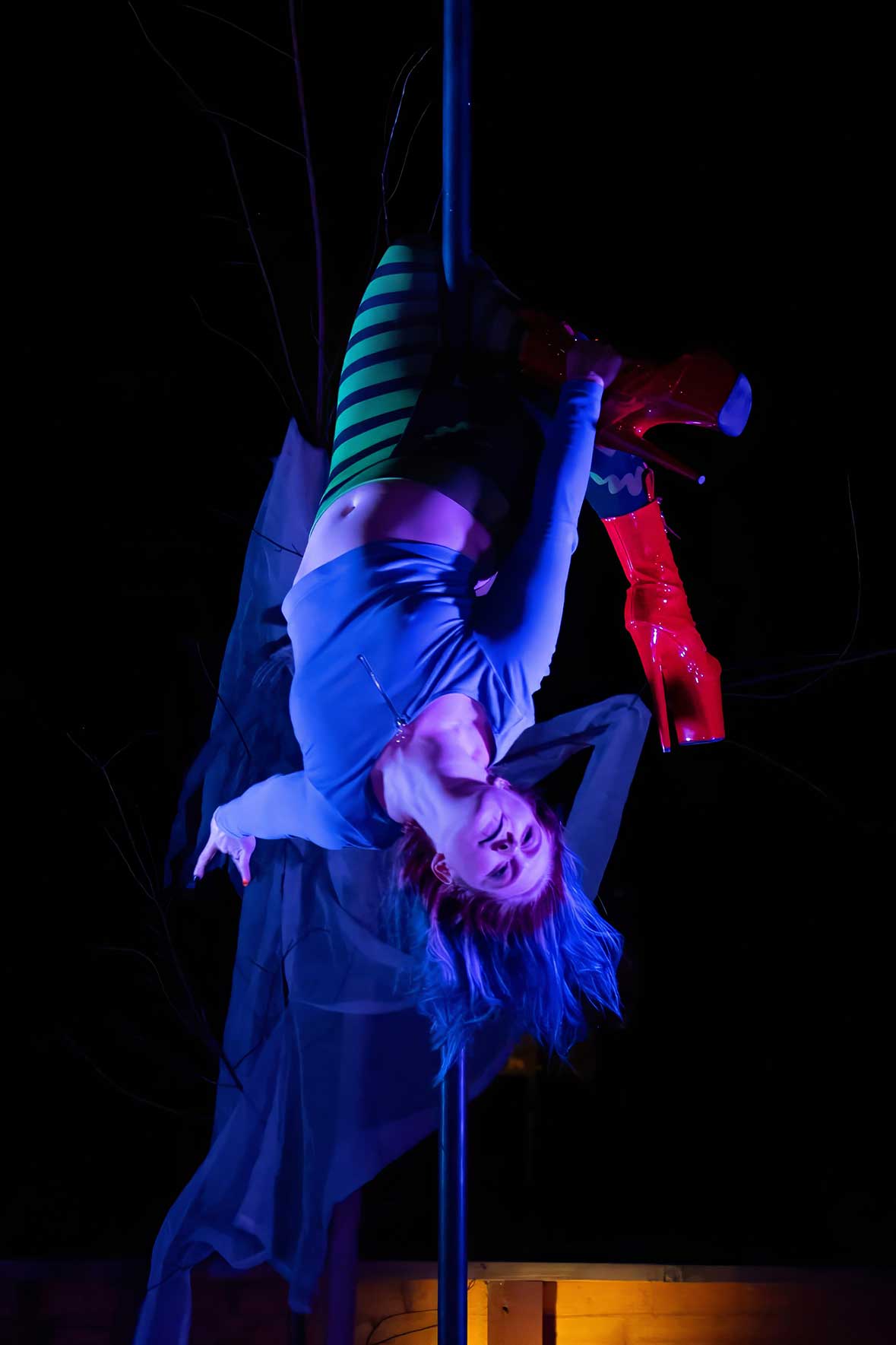 Pole dancer hanging upside down in blue and purple lighting