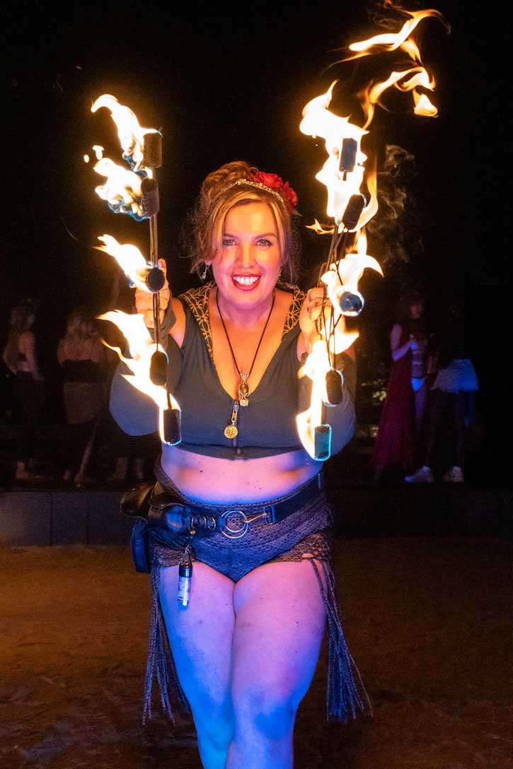 Smiling woman spinning multiple flaming fire fans at night