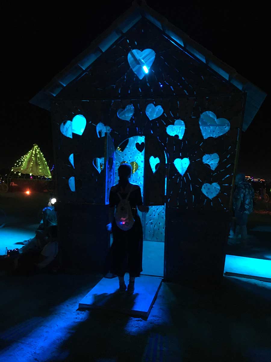 Silhouetted figure inside glowing blue heart-shaped house installation