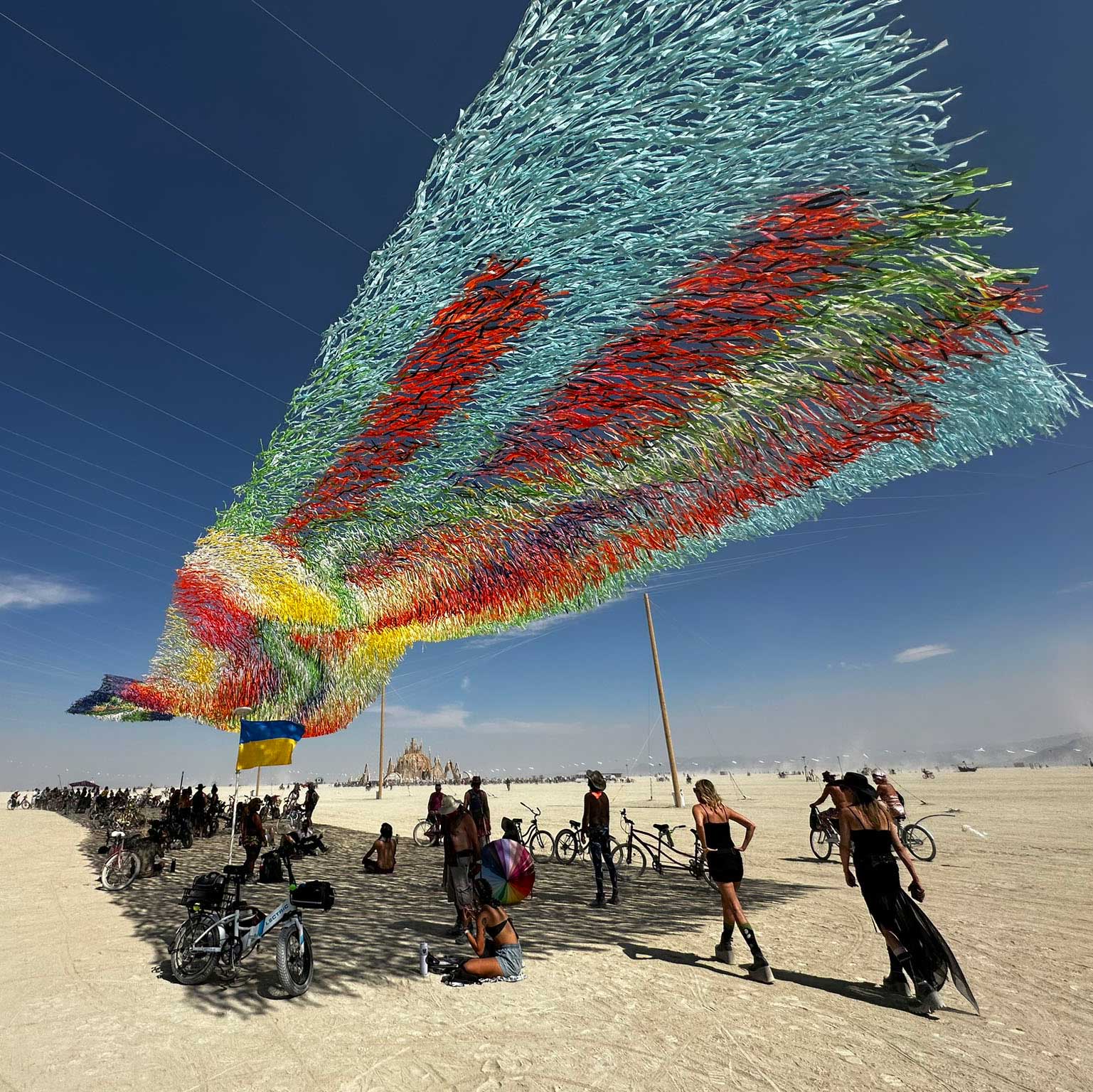 Massive colorful feathered wing sculpture soaring over Burning Man playa
