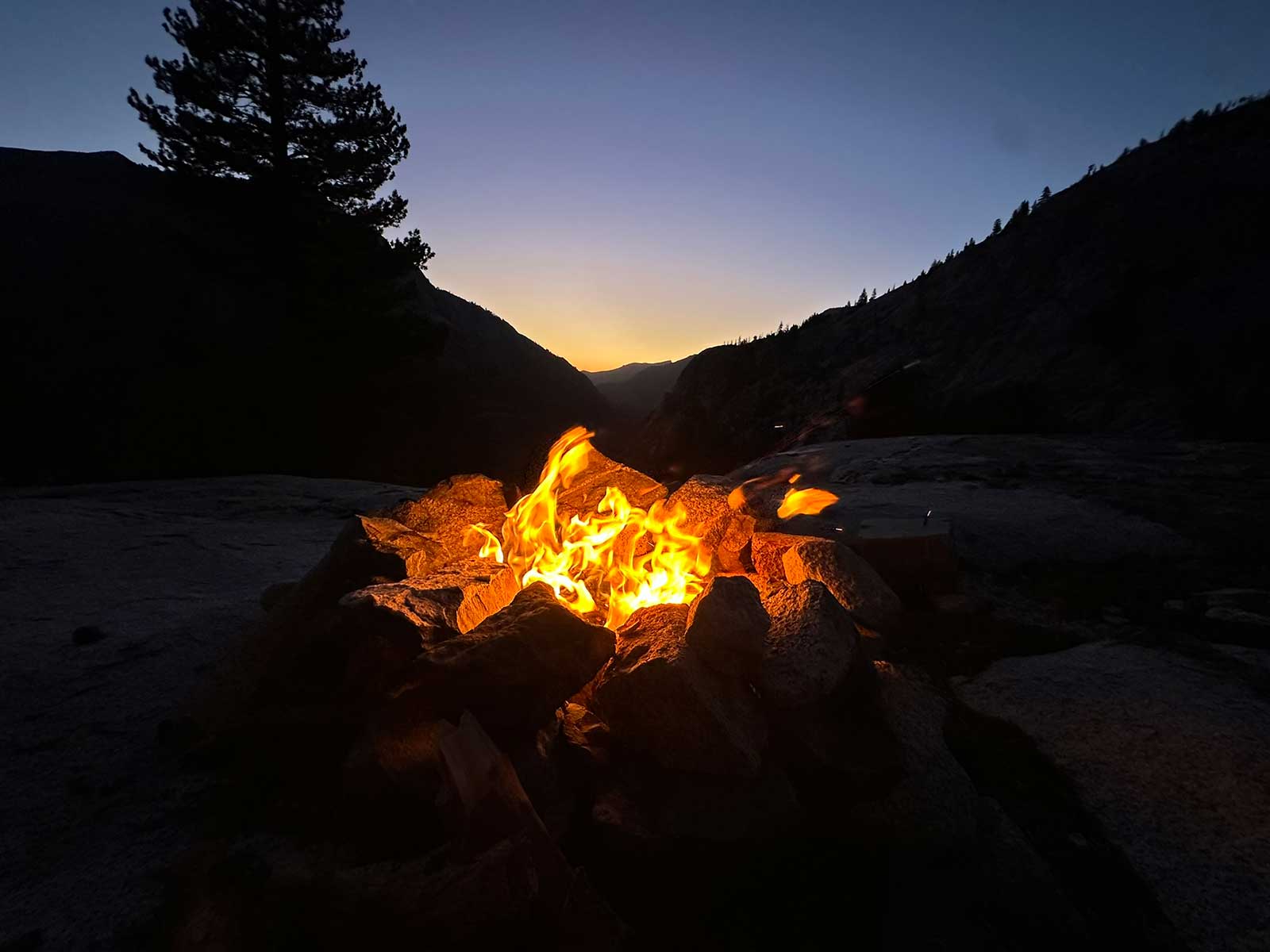 Campfire blazing in stone ring at mountain canyon dusk