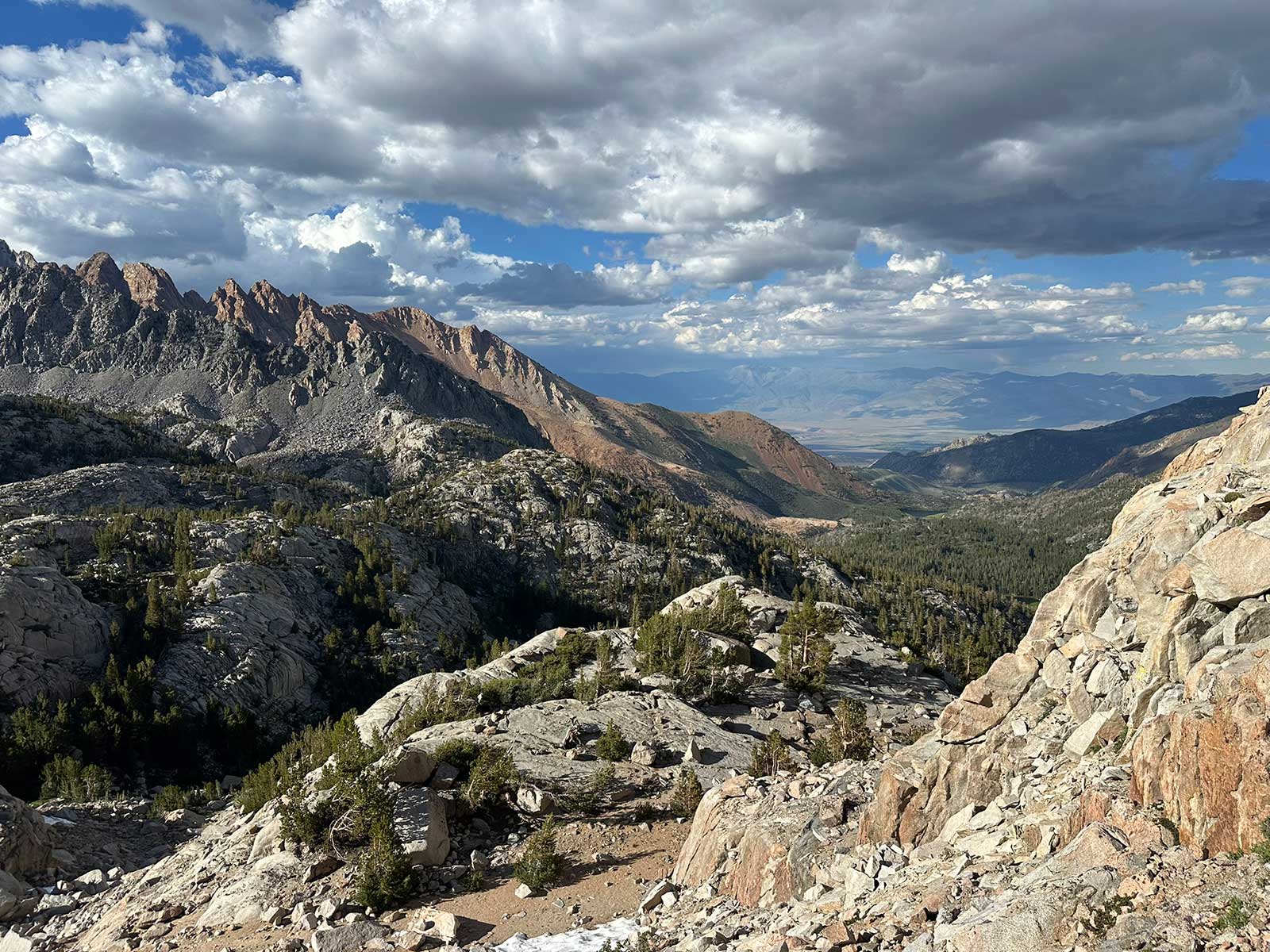 Jagged granite peaks above pine forest valley and distant plain