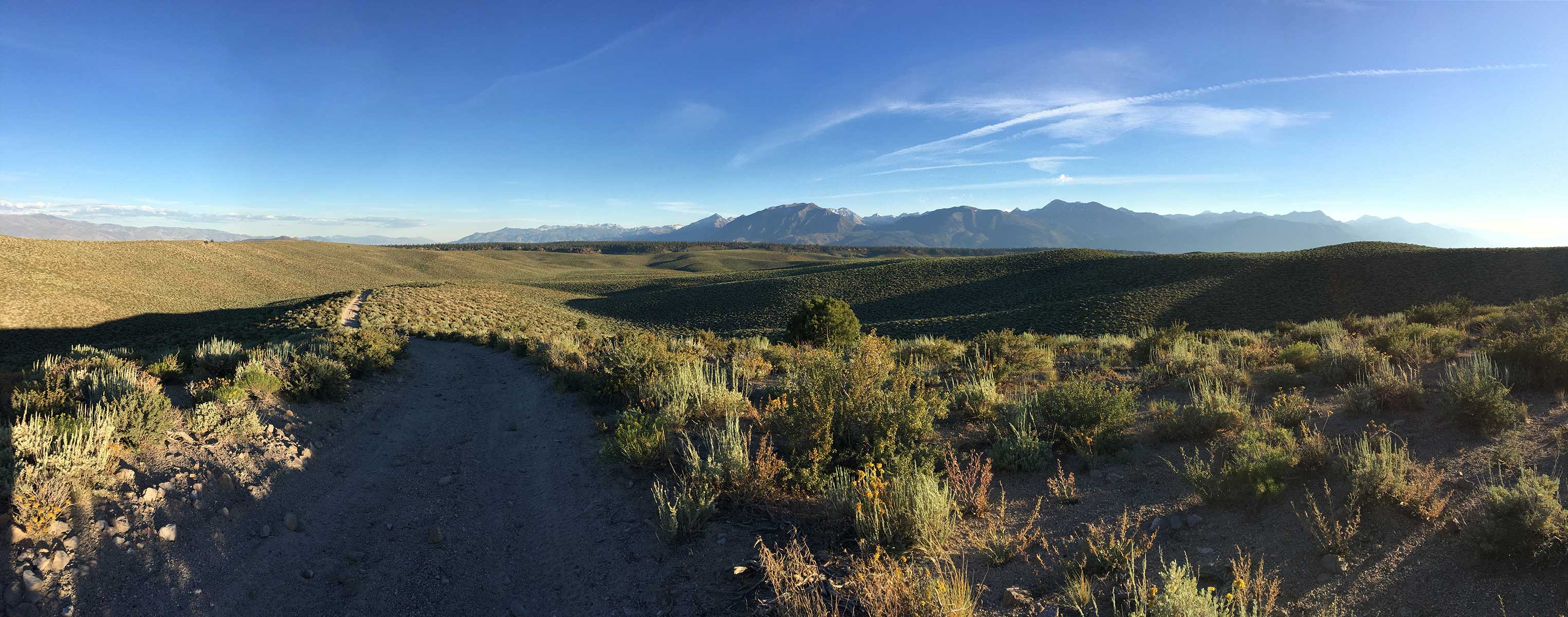 Panoramic sagebrush desert road toward snow-capped mountains