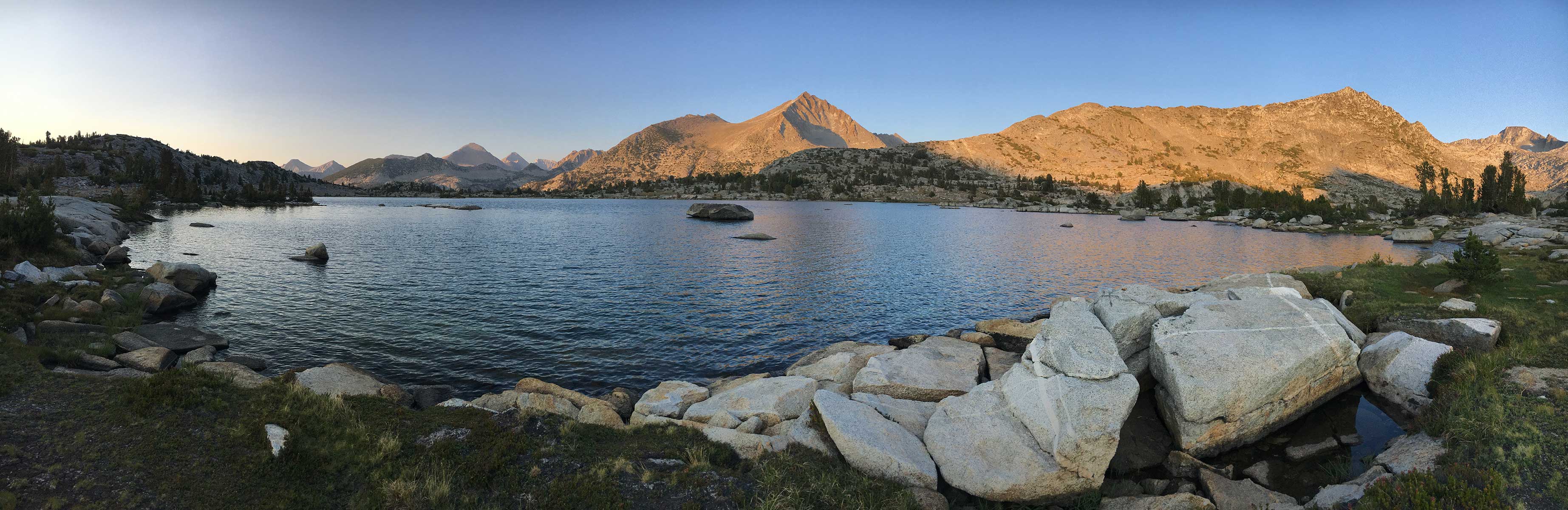 Panoramic alpine lake ringed by golden granite peaks at sunset