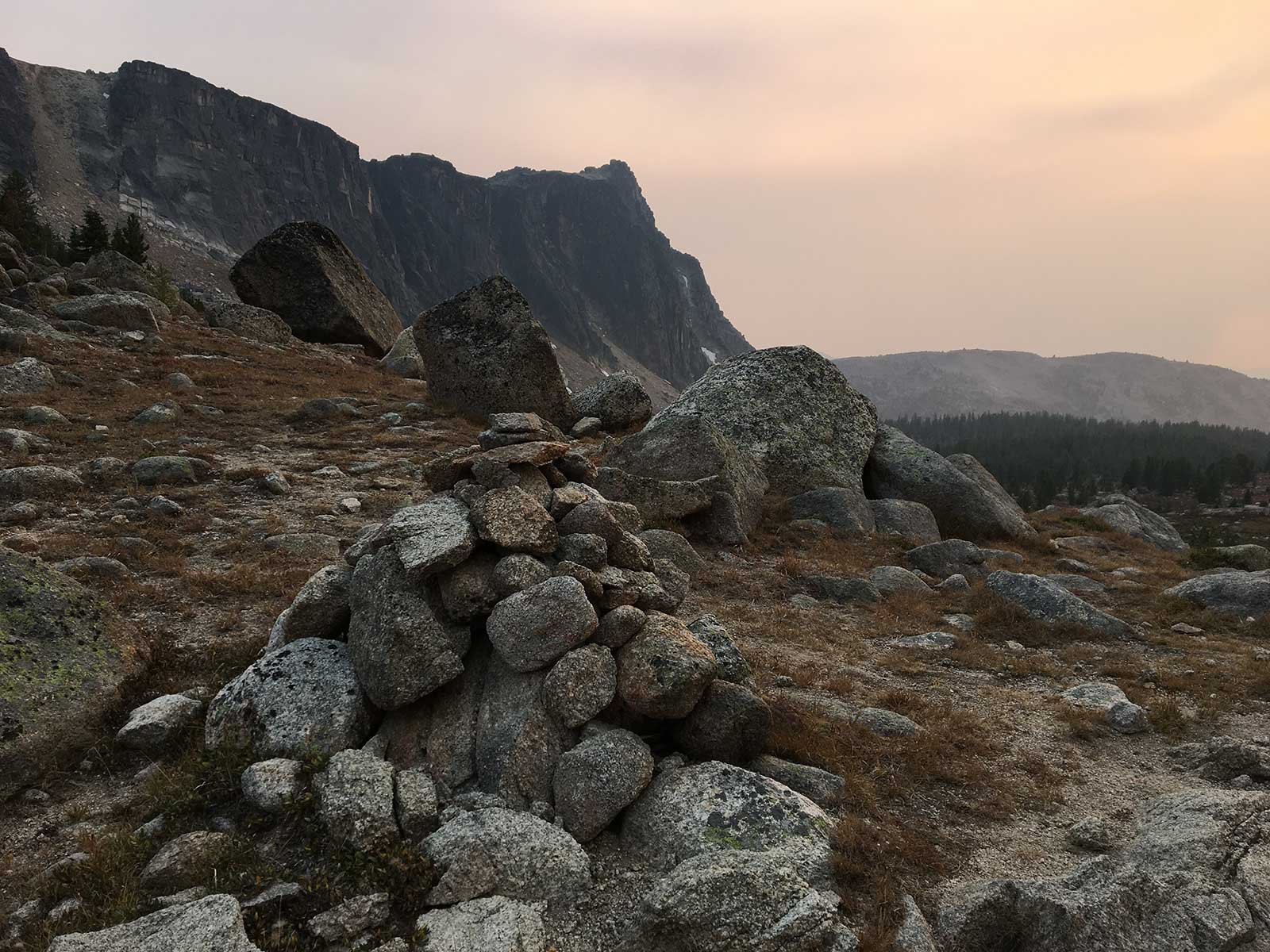 Stone cairn on rocky alpine slope at smoky sunset