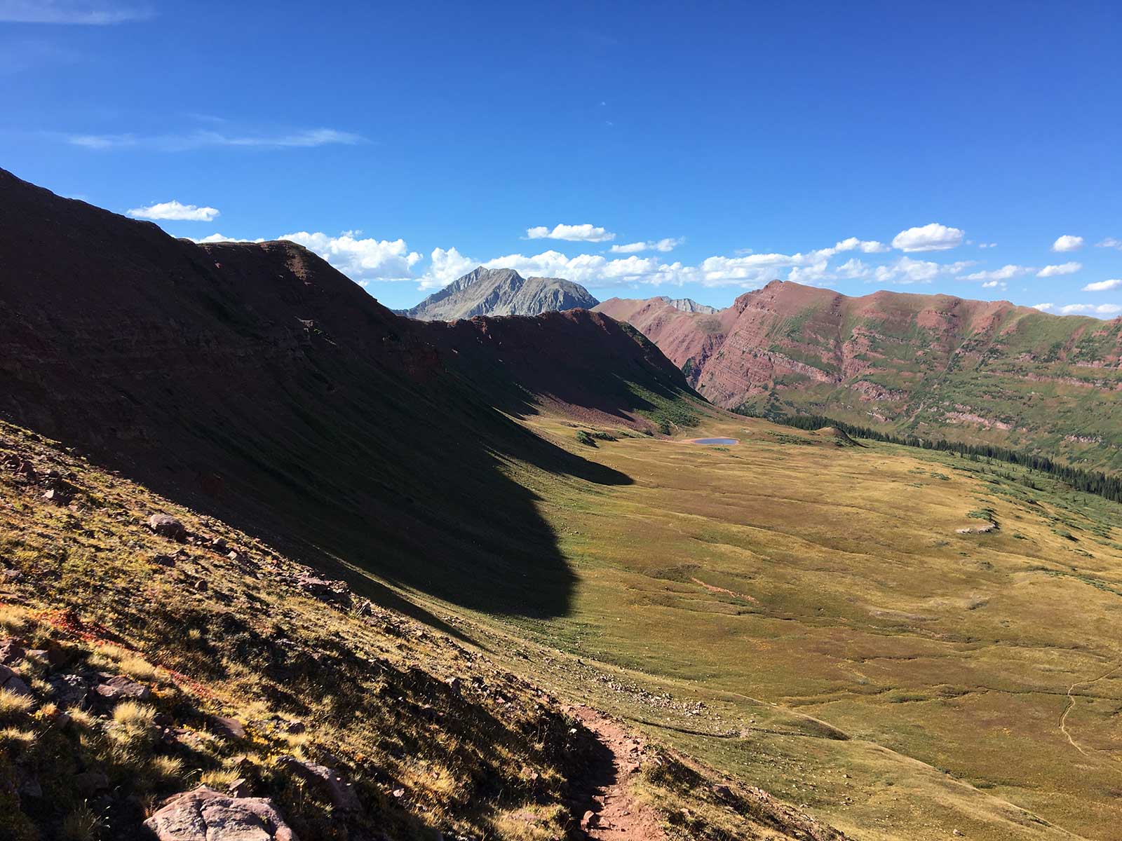 Broad alpine valley with colorful slopes and small tarn below
